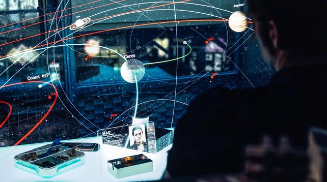 A screenshot from the TV series The Expanse showing a solar system star map seemingly projected over a table with various celestial bodies and orbits, and the character of Miller seen from behind on the right.