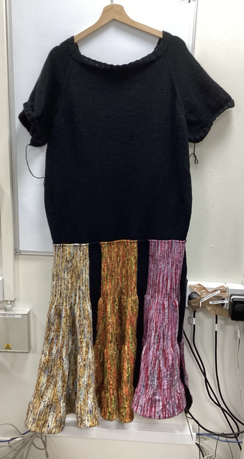 Three  coloured sections of a knitted dress. Left to right, the first section white and brown with some blue spots. The second section is red, yellow and orange with spots of green. The third section is red and pink tones.