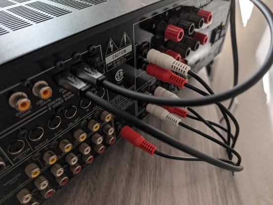 A partial angled rear view of the receiver in the first post. Various audio cables are attached, including two optical cables and six RCA cables.