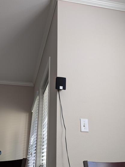 A lonely rear satellite speaker mounted on a wall. The cable for it is dangling ungracefully downwards at an angle.