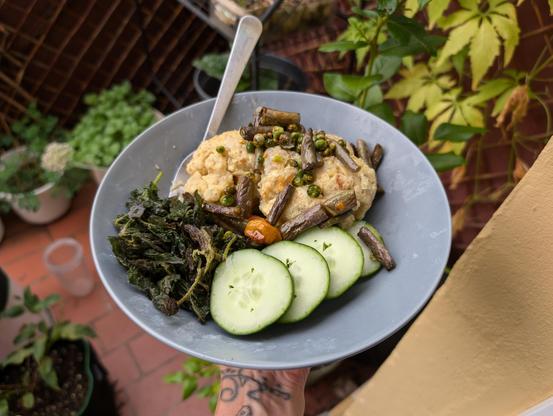 Plate with the food described in the post held by a person with a tattoo on her wrist. In the background are plants on a balcony.