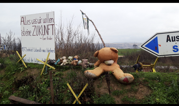 In der Nähe der abrisskante vom tagebau lützerath kurz vor der Räumung des Dorfes. Die geben x für den Tag X. 
Ein grosser Teddybär mit eingesunkenem Kopf sitzt dabei. Viele Kuscheltiere,  teils schon arg ramponiert, liegen auch an dieser Stelle?. Es sind aus den vom Abriss bedrohten Häusern zurückgelassen kuscheltiere. Auf einem Schild steht: alles. Was wir wollen, ist eine Zukunft.

 eure Kinder