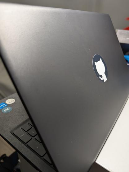 A picture showing a laptop with a GitHub logo sticker in the place of the Dell logo on the back and arduino stickers below the keyboard