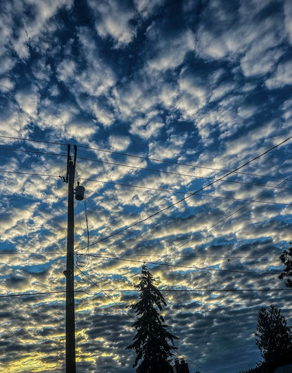 White clouds filled blue sky with a electric pole on the left and electric wires  across the frame 