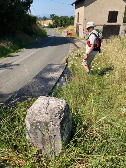 A border stone in the foreground showing the wiggly line on top that indicates that the border follows the road (entirely in France here)