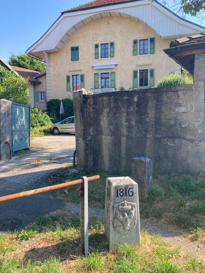 The  other side of the border stone, showing the Sardinian heraldry, now part of France, with a large house in the background. This site was much used in WWII as a point for smuggling refugees- Jewish & others - into Switzerland.