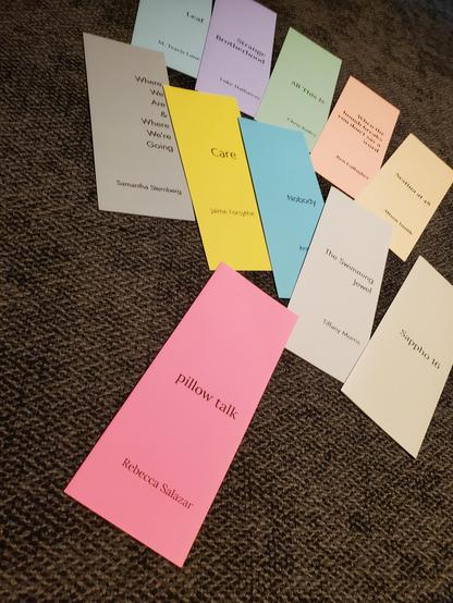 Many colourful Opaat Press poetry pamphlets are arranged on a gray carpet, with pillow talk by Rebecca Salazar in neon pink at the front.