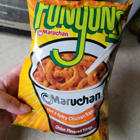 Hand holding a small bag of Funyuns, with a Maruchan Hot & Spicy Chicken Ramen flavor.