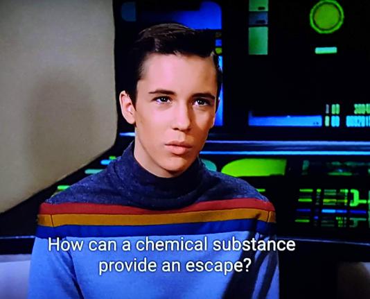 TNG scene. We're on ship and see young Wesley Crusher wearing his trademark blue / blue / orange / red / blue sweater, while seated at a computer console. He's turned around and chatting with someone, hopefully a responsible adult who can turn this into a real teachable moment. Closed caption reads, "How can a chemical substance provide an escape?"