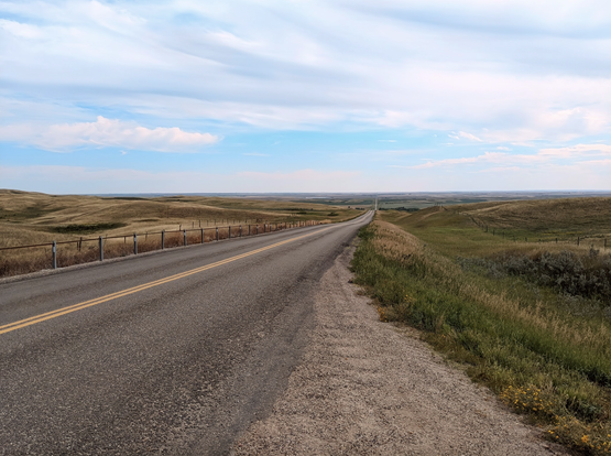 rural prairies in canada, highway extends into the horizon, hills of green and yellow. summer.