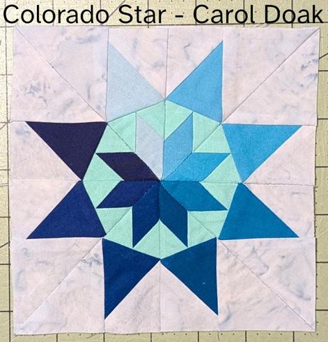 A quilt block with an 8-pointed star, done in blue fabric.  The background is a light blue-grey marble.  Each point of the star forms a gradient, with light blue in the upper left, darkening back around to navy blue right next to that light blue in the upper left.