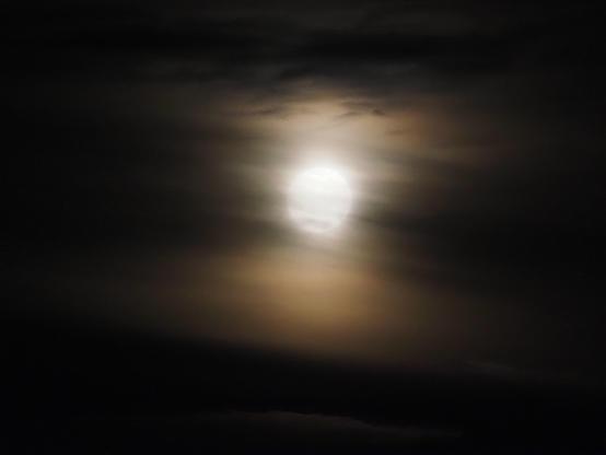 Der Mond etwas verwaschen hinter Wolkenschleiern, die durch das Licht des Mondes in Beige- und Brauntönen zu sehen sind.