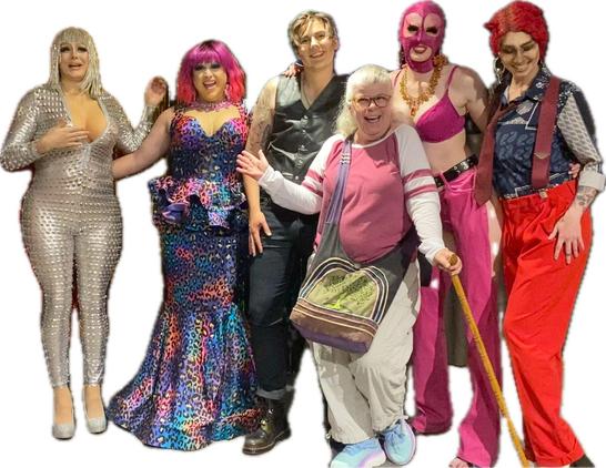 Group of 3 drag queens and 2 kings behind a chubby old woman with grey hair leaning seductively on her cane. L-R: Wanda Lust in a sequined silver outfit and wig, Freida Whales in red wig, colorful mermaid style blue & pink gown, Peter Packer in leather, me, Fuschia in red head cover & bra and okay, call it ‘fuschia’ red pants, Other Earth in red wig with horns, suspenders holding up bright red pants, all smiling. #DragIsArt