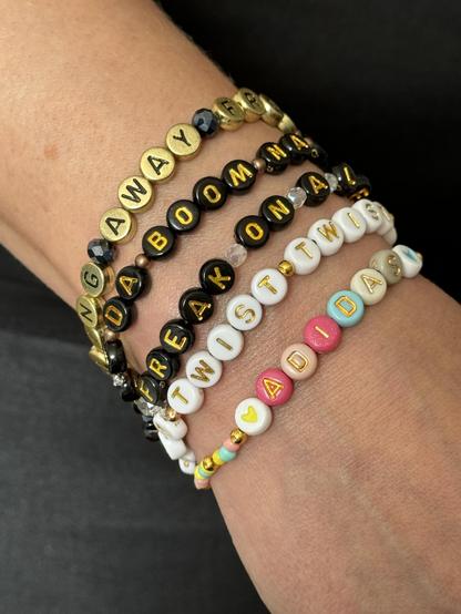 A wrist with 5 friendship bracelets with letter beads. The letters form the lyrics and names of songs by the band Korn: Freak on a leash, Falling away from me, Da boom na da oom na na ema go, Twist and ADIDAS.