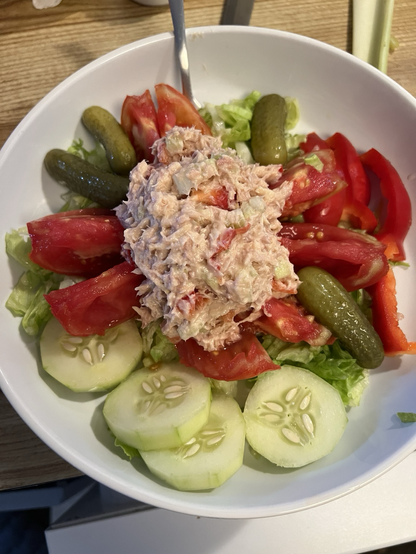 A heap of tuna salad atop a homegrown tomato cut like a star with fresh cucumber, red bell pepper & baby dill pickles on a bed of shredded lettuce. 