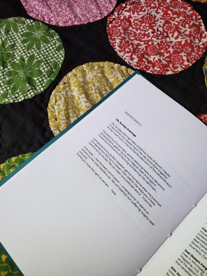The poetry collection/chapbook Pinhole Poetry Volume Two Selected sits on a colourful quilt, open to a selected poem.