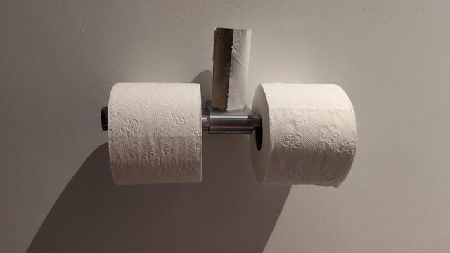 Zwei volle Klopapierrollen nebeneinander hängend, dazwischen aufrecht stehend eine leere Klopapierrolle.