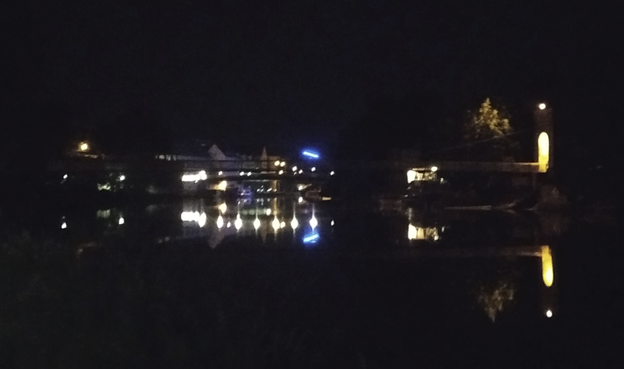 Blick von der Hiroshima-Wiese zur Drahtbrücke. Eine blaue Leuchte hängt über der Fulda.