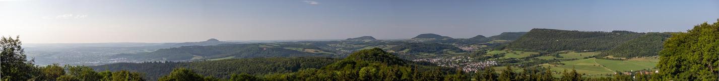 Blick in die Landschaft vom Aussichtpunkt aus.
Man sieht die Ebene Richtung Stuttgart, dann drei markante steile Hügel in einigen Kilometern Entfernung, die früher Vulkane am Albtrauf waren: Die Drei Kaiserberge Hohenstaufen, Rechberg und Stuifen. Weitblick.