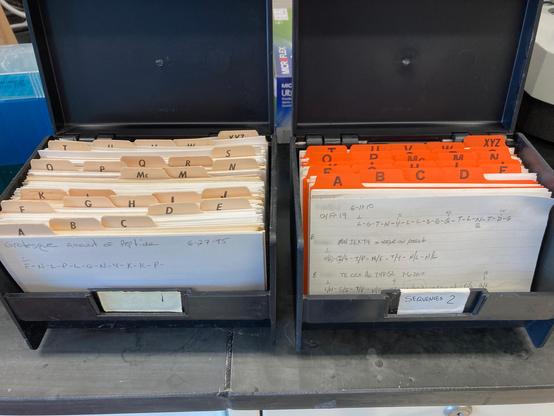 Two large black index card boxes filled with cards each with one or more results from automated Edman sequencing written out in single letter code.  On the left is a card with the title "Grotesque amount of peptide" and the amino acid sequence written below.  The title sarcastically reflected the very large quantity that was subjected to Edman sequencing which maxed out the detector for each sequencing cycle.  On the right side is another card file and the first card shows 3 amino acid sequences determined from proteins isolated from electrophoretic gel separation and subsequent enzymatic digestion and sequencing of the resulting peptides.