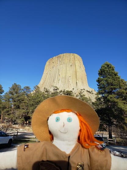 Ranger Sarah a redhead doll dressed like a park ranger stands in the bottom center with Devils Tower behind her