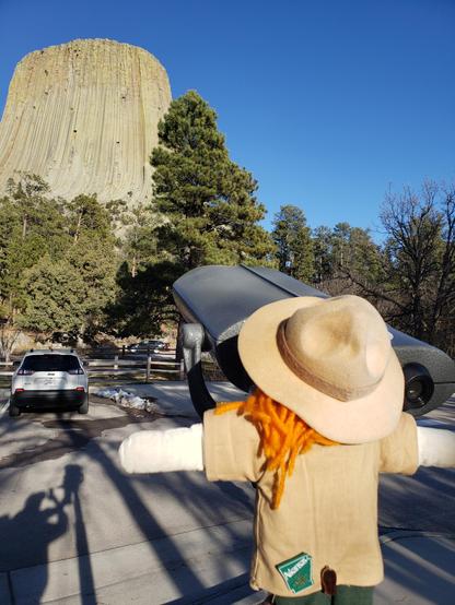 Ranger Sarah a park ranger doll with red head in the bottom right looks at Devils Tower through binoculars