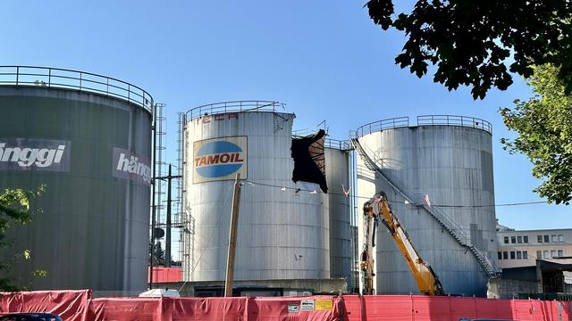 Tanklager mit grossen Silos aus glänzendem Metall. Der Bagger hat ein Drittel aus einem Silo herausgeschnitten.