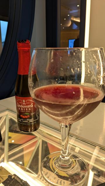 A goblet containing Lindeman's Kriek, the bottle can be seen in the background