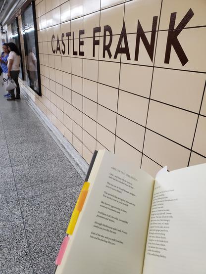 Poetry collection No Meeting Without Body by Annick MacAskill (Gaspereau Press), opened to the poem "Ode on the Afternoon", with colourful post-it notes protruding from the book, is held up against the wall of Toronto's Castle Frank subway station (which is mentioned in the poem)