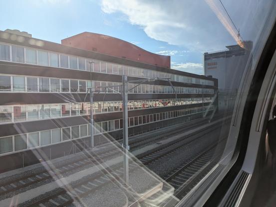 Un immeuble de bureaux le long de la voie ferrée à hauteur de Renens. Dans les vitres des bureaux on devine le reflet du train FV Dosto qui assure une liaison IC 1 en direction de Genève.