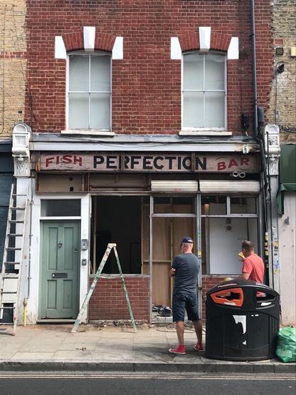 Workers standing in front of a terraced building with a shop on the ground floor. A ladder is also visible, and windows and doors have been removed from the shopfront. Above this is an old fascia sign with 'perfection' in black across most of its width, flanked by 'fish' (left) and 'bar' (right) in red.