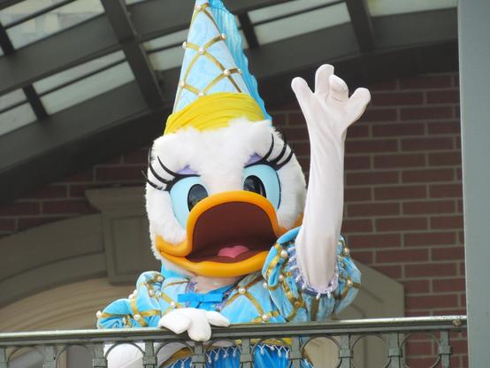 Photo of Daisy Duck dressed as a princess and waving from the second level of the Main Street train station at Walt Disney World's Magic Kingdom