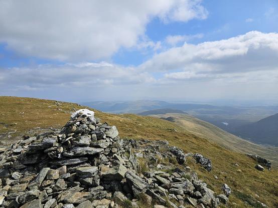 Cairn at the top of a Scottish Munro with blue skies and long views over other hills.
