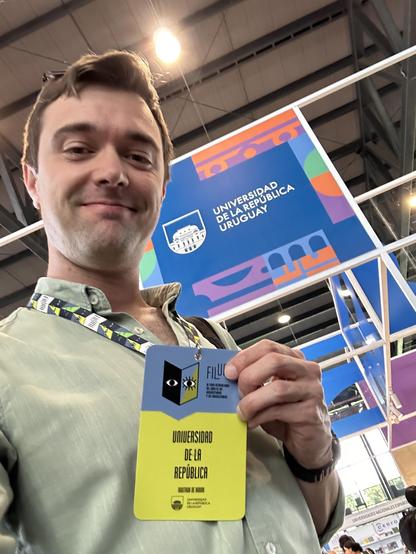 Me showing my accreditation to FILUNI as part of the Udelar delegation. Behind me, the Udelar stand.