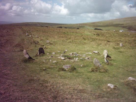 Looking down on of the the double stone rows from the cairn circle at Merrivale on Dartmoor in Devon. The undulating moors stretch into the distance and the sky is full of grey clouds.
