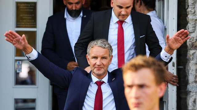Foto van Björn Höcke, lijsttrekker van de AfD in Thüringen, die tussen partijgenoten (?) naar buiten komt, met zijn beide armen schuin omhoog gestrekt
(Reuters)  
