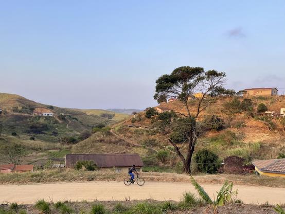Rural landscapes in the background, a man on a bycicle on a dust road in the foreground, afternoon warm light
