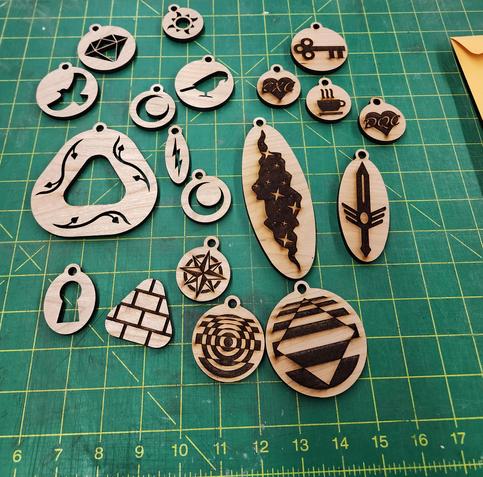Assorted wooden pieces with holes through:
Diamond, sun, bird in flight, stylized moon, parrot, lightning, stylized moon (again), triangle with leafy vines, keyhole
Assorted wooden pieces with etched patterns:
Key, hearts with CXC and DQC, hot mug, starry expanse, winged sword, compass rose, overlapped concentric circles, overlapped square, brick wall