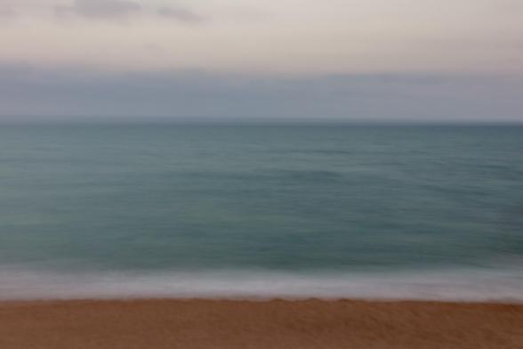 Fotografía usando larga exposición y moviendo ligeramente la cámara donde se ve el mar en una gran franja central y en la parte inferior, algo de tierra de la playa mientras en la superior un algo del cielo difuminado.