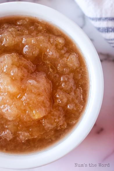A small bowl of homemade Crockpot Applesauce. The applesauce is a lovely golden color in a white bowl. The photo is zoomed in close so you can see that the applesauce was left a little chunky.