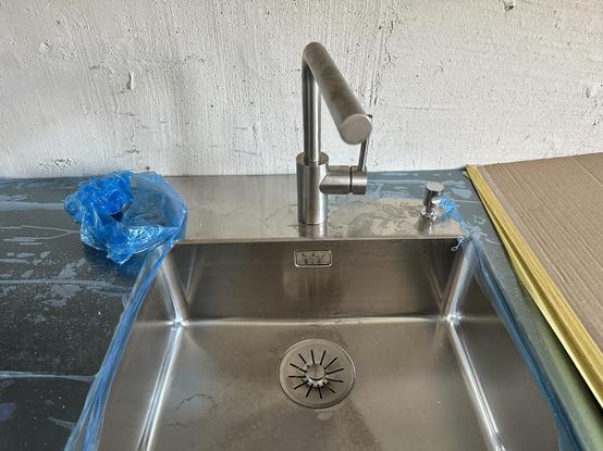 Spüle mit Wasserhahn, rundherum noch Rohbau bzw. Kunststoff- und Kartonabdeckungen.