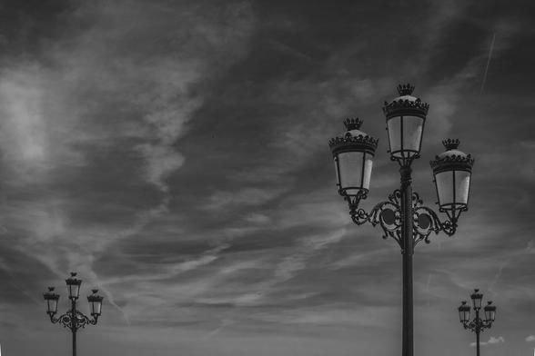 Fotografía en blanco y negro donde se ven tres farolas que a su vez cuentan con tres faroles.