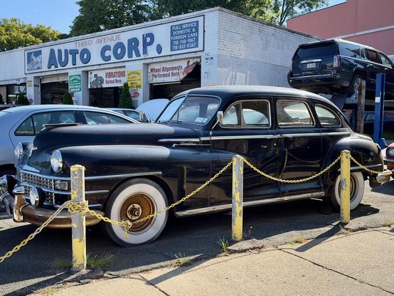 An old car in a mechanic’s parking lot.