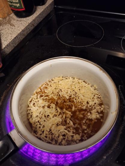A white pot on a lit stove is filled with grated beeswax and brown liquid