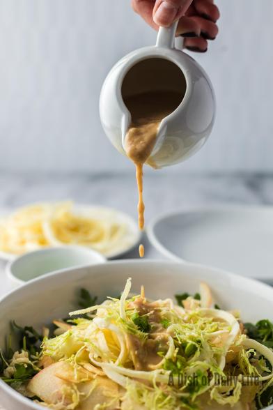 Apple and Parsnip Power Bowl - also known as a healthy salad - is in a bowl with salad dressing being poured over the top. 