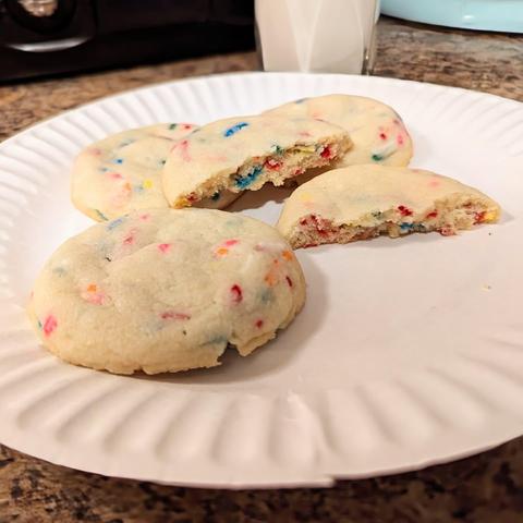 Image shows 4 cookies with sprinkles in them on a white paper plate.