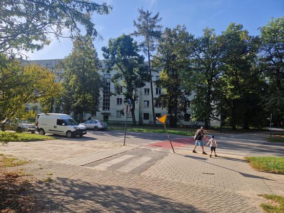 Przejście dla pieszych między parkiem a placem zabaw. Samochód dostawczy jest zapakowany mniej niż obowiązkowe 10m. Jeden ze znaków jest pochylony, prawdopodobnie został potrącony przez pojazd. 