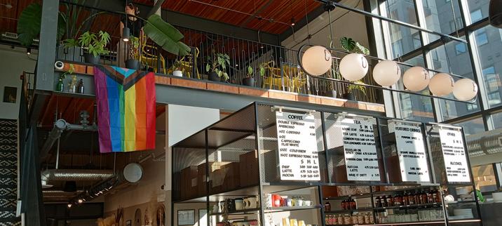 very tall, spacious and light filled cafe. pride flag hanging from the loft space beside the order boards. large lit up orbs like an old time lamp post spell out C O F F E E. It looks as beautiful as it tastes.