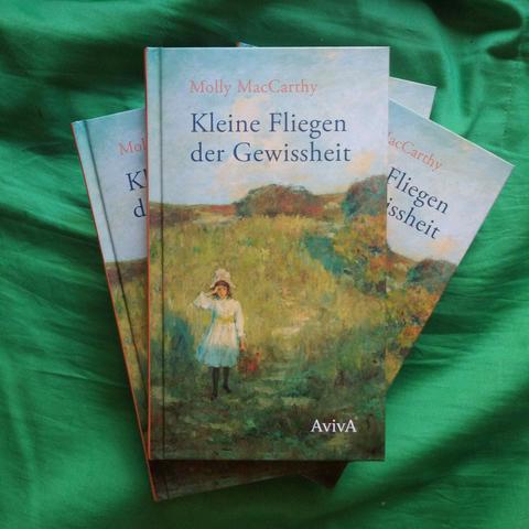 Vier Exemplare des Buches Kleine Fliegen der Gewissheit liegen, halb übereinander, auf einem grünen Tuch.