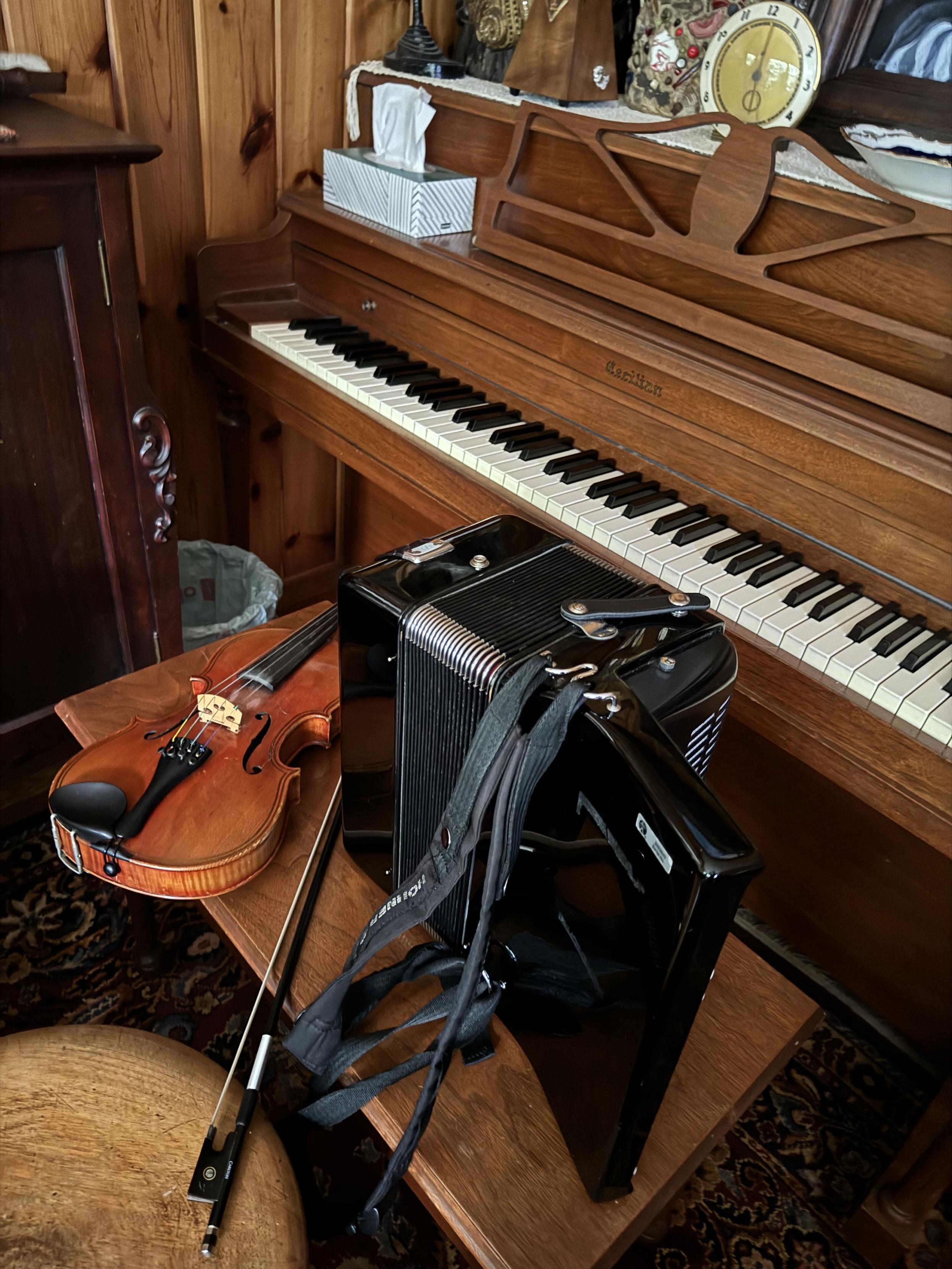 A violin and an accordion sitting on a piano bench 